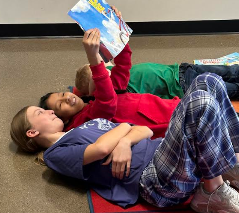 Three students laying on the floor reading to eachother.