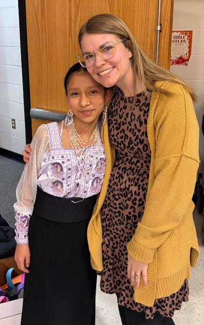 A student smiling in her traditional Ecuadorian dress before her concert. She is with her teacher in the photo.