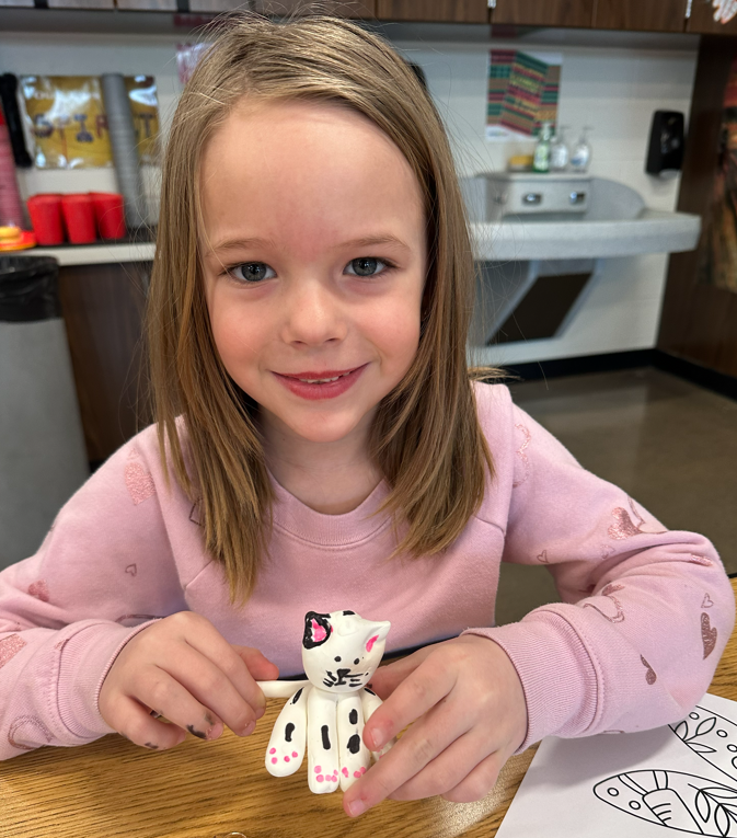 A little girl with her sculpture of a cat.
