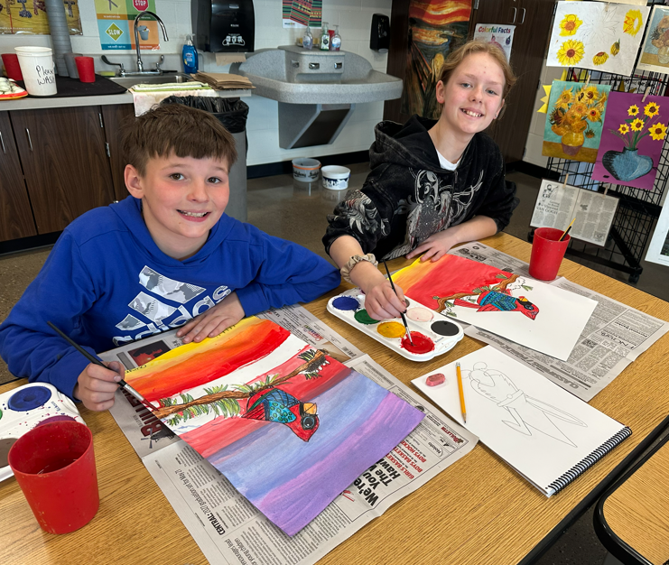 Two students smiling and painting.
