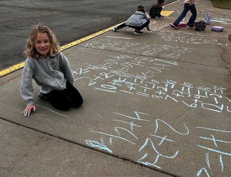 A little girl working on math facts on sidwalk.