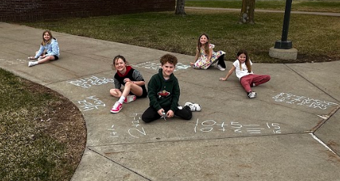 Group of students with sidewalk chalk and sitting down smiling.
