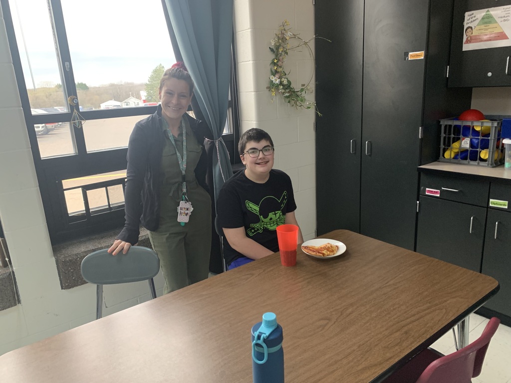 A staff member and student smiling with pizza.