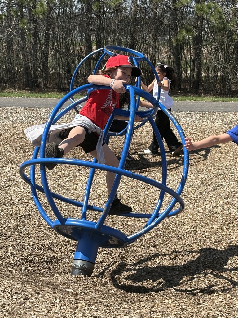 A little boy spinning on playground equipment.