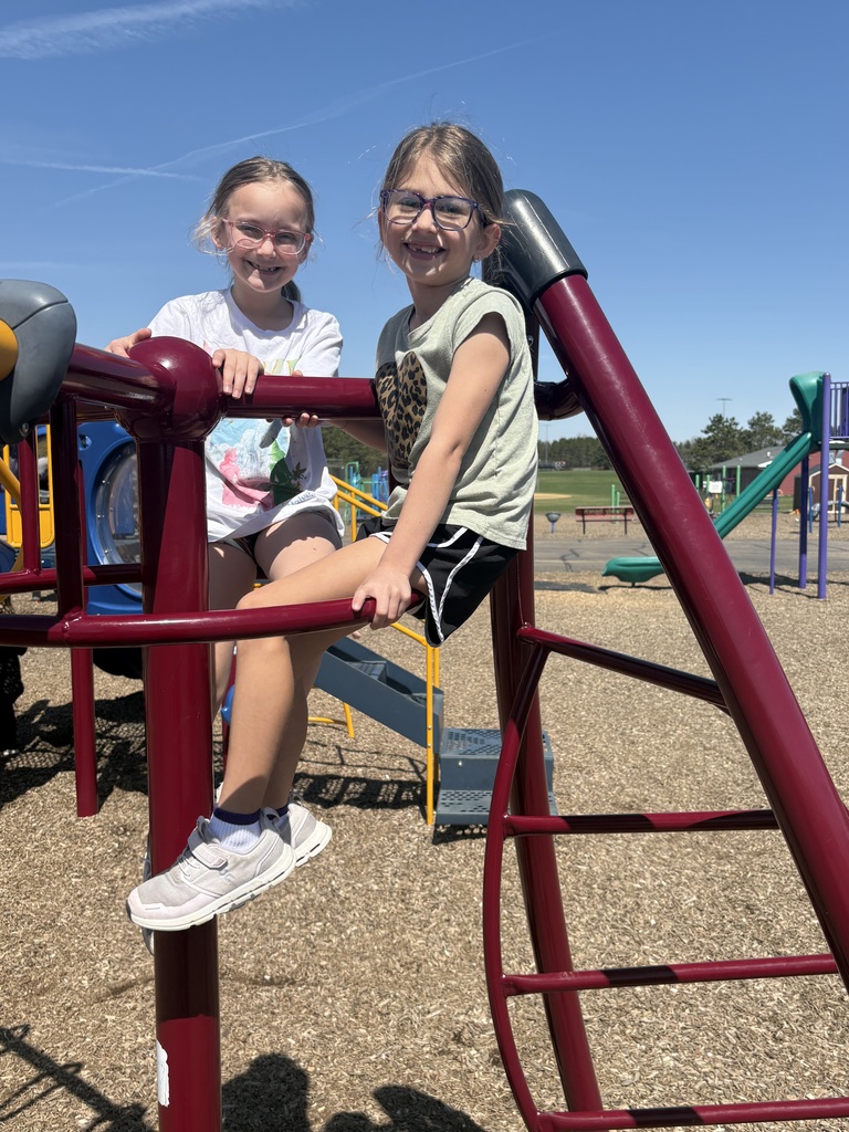 Two girls sitting on the playground equipment smiling.