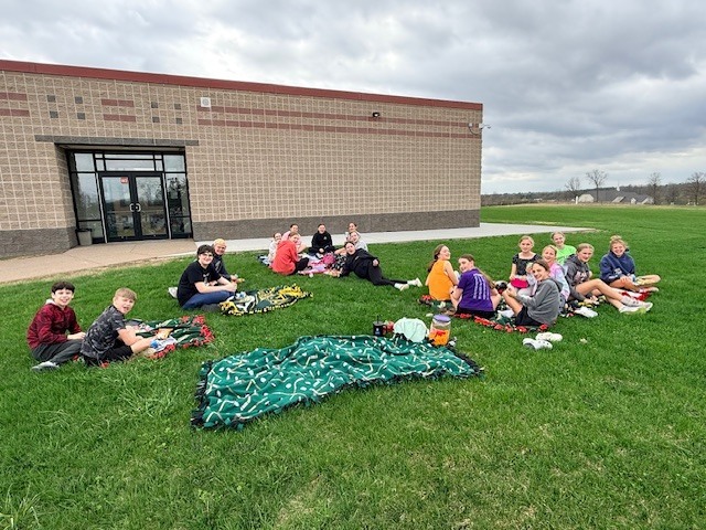 Students sitting outside on their blankets eating lunch.