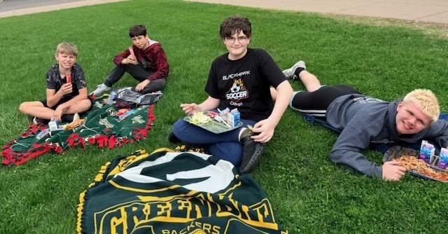 Four boys sitting on the grass smiling.