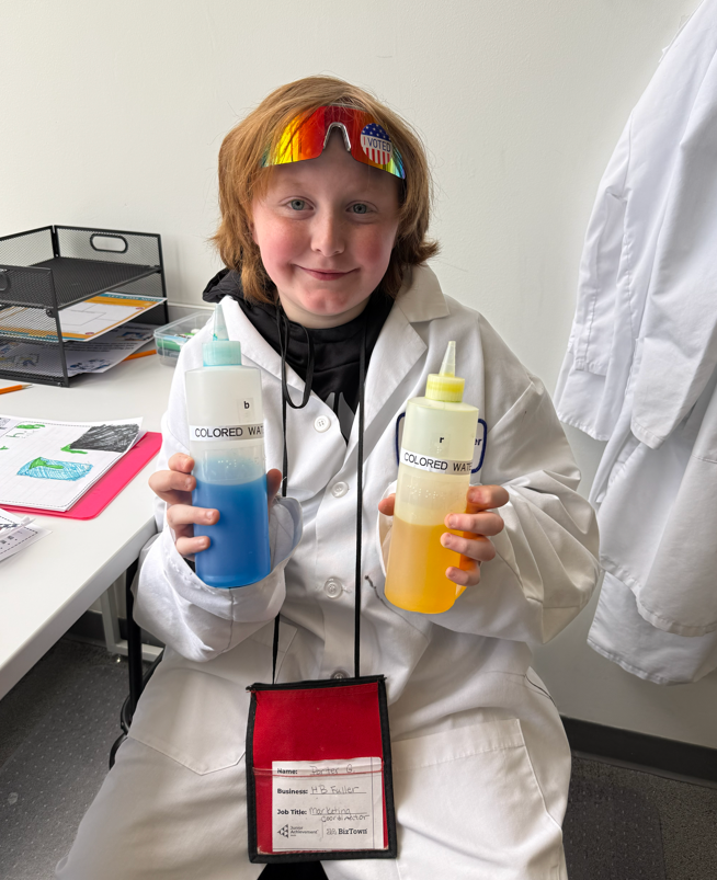 Student smiling with two different bottles of water with food coloring.