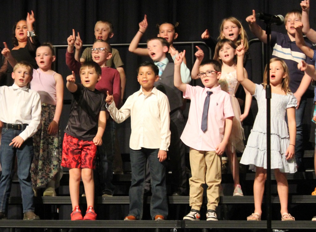 Students standing and singing with a #1 finger up in the air.