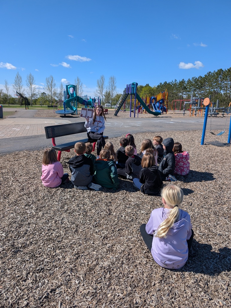 Students sitting outside listening to the teacher read.