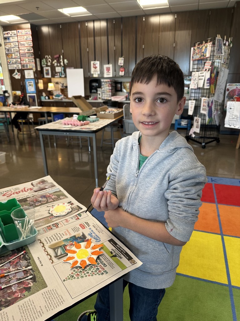 A boy smiling while painting a clay sun.