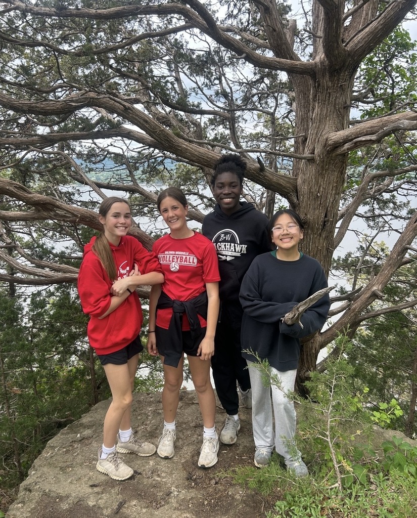 Four students on a hike, smiling by a tree.