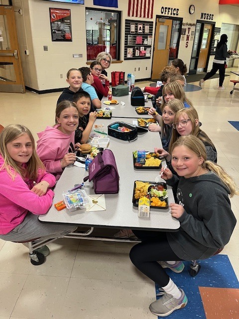 5th graders anda  teacher sitting at the lunch table.