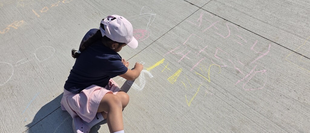 A little girl writing math problems on the sidwalk