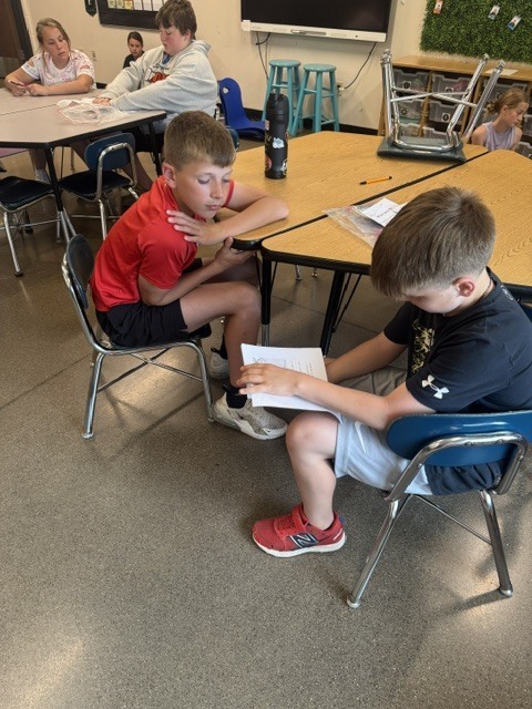 A student leaning and listening to someone read to him.