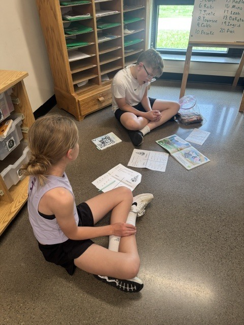 Two students sitting on the floor looking at a book.