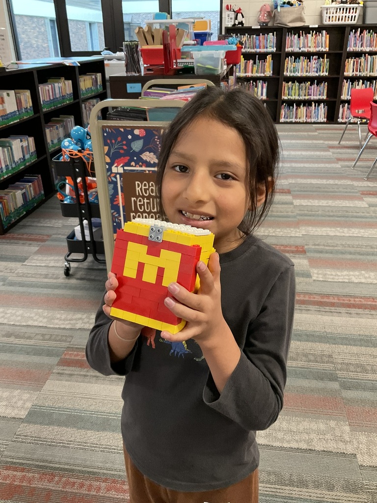 A student smiling with their red and yellow lego creation.