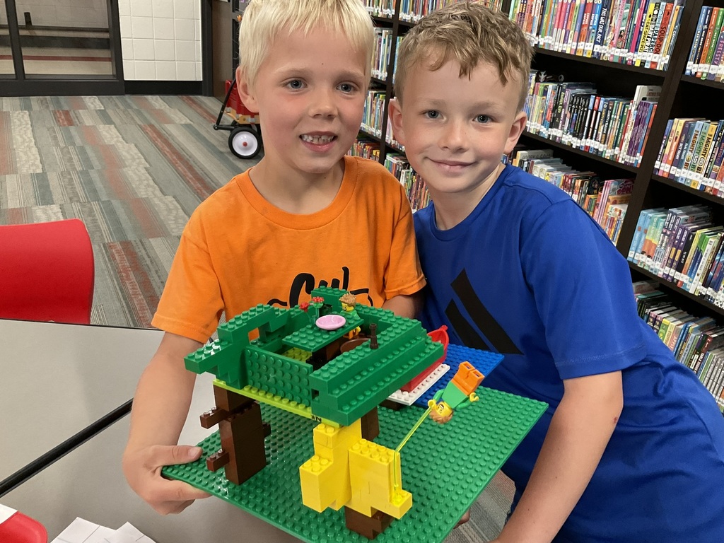 Two boys holding a lego creation and smiling.