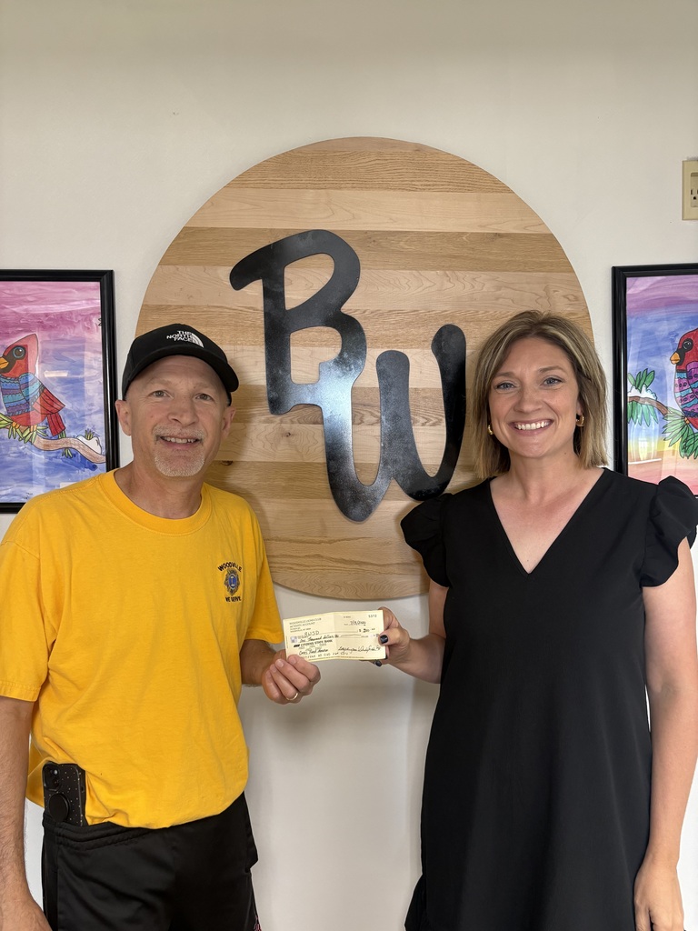 Woodville Lions Club member Steve Perry presenting a donation check to Kelsey Brewer in front of a wooden Baldwin-Woodville "BW" emblem.