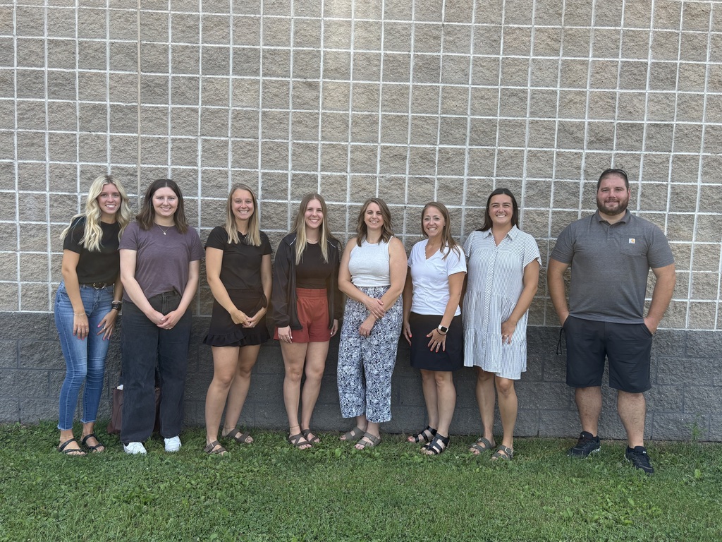 Line of teachers smiling in front of the building.