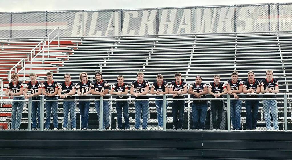 Senior football players leaning on the fence of the bleachers.
