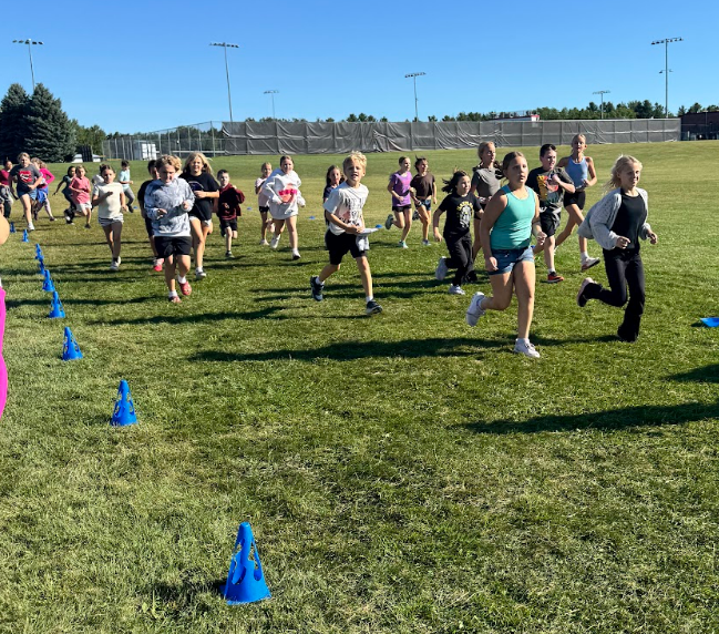 Students running and walking outside around blue cones.