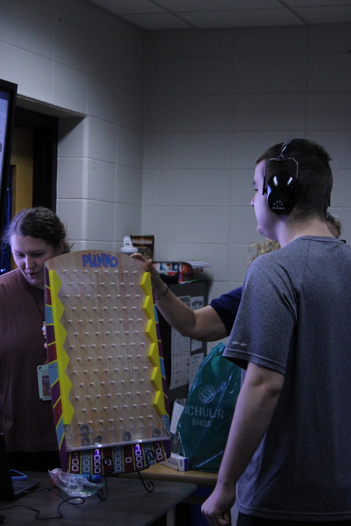 A student preparing to drop a chip down a custom tabletop Plinko board held by a staff member during a classroom gam