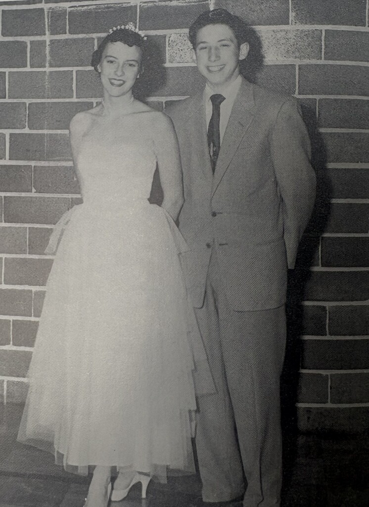 Black-and-white vintage photo from a past Baldwin-Woodville yearbook showing a smiling Homecoming couple standing against a brick wall.