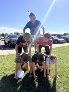A small group of cross country teammates forming a human pyramid together outdoors on a sunny day during team-building games.