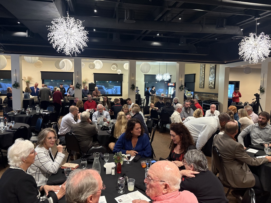 Guests seated at round tables during a banquet event with a presentation screen displaying "Hall of Fame" in the background.