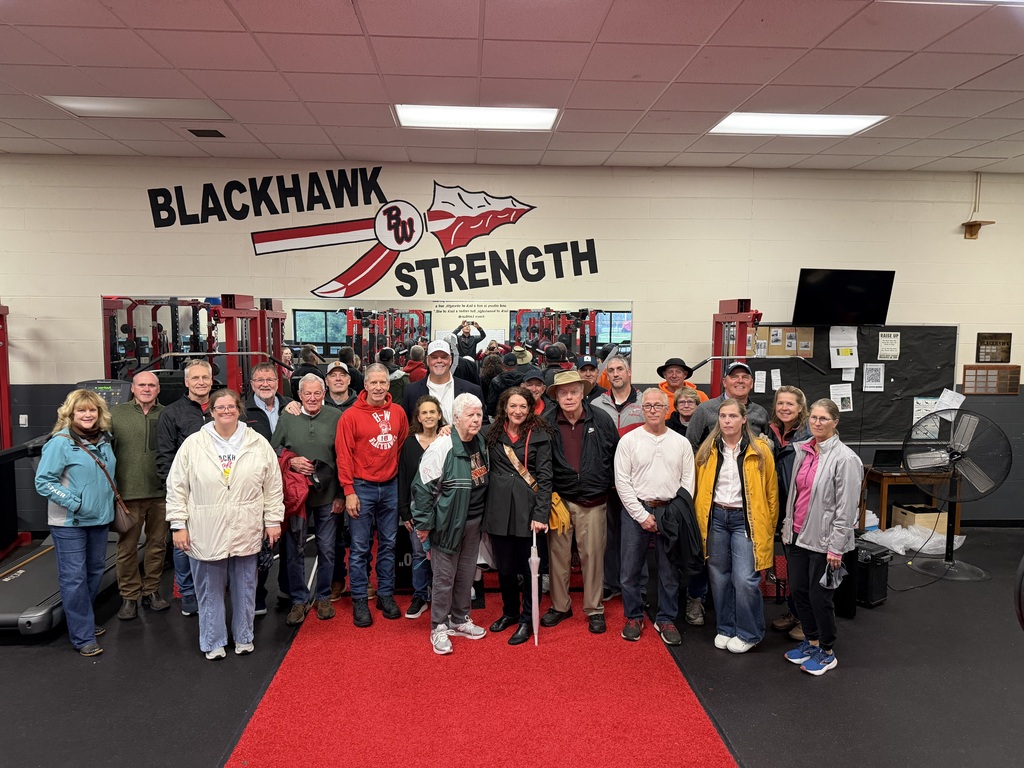 A large group of attendees posing together on a red runner inside a gym facility under a wall decal reading "Blackhawk Strength."