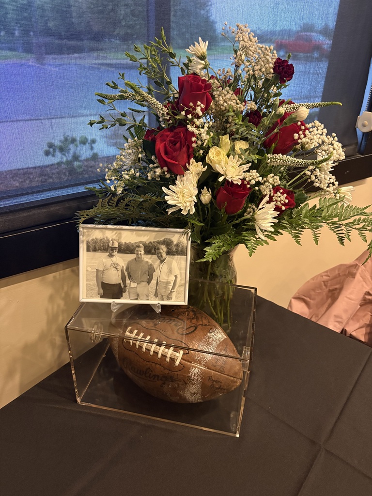 A floral arrangement of red and white flowers next to a framed black-and-white photo and a signed football inside a clear display case on a table.
