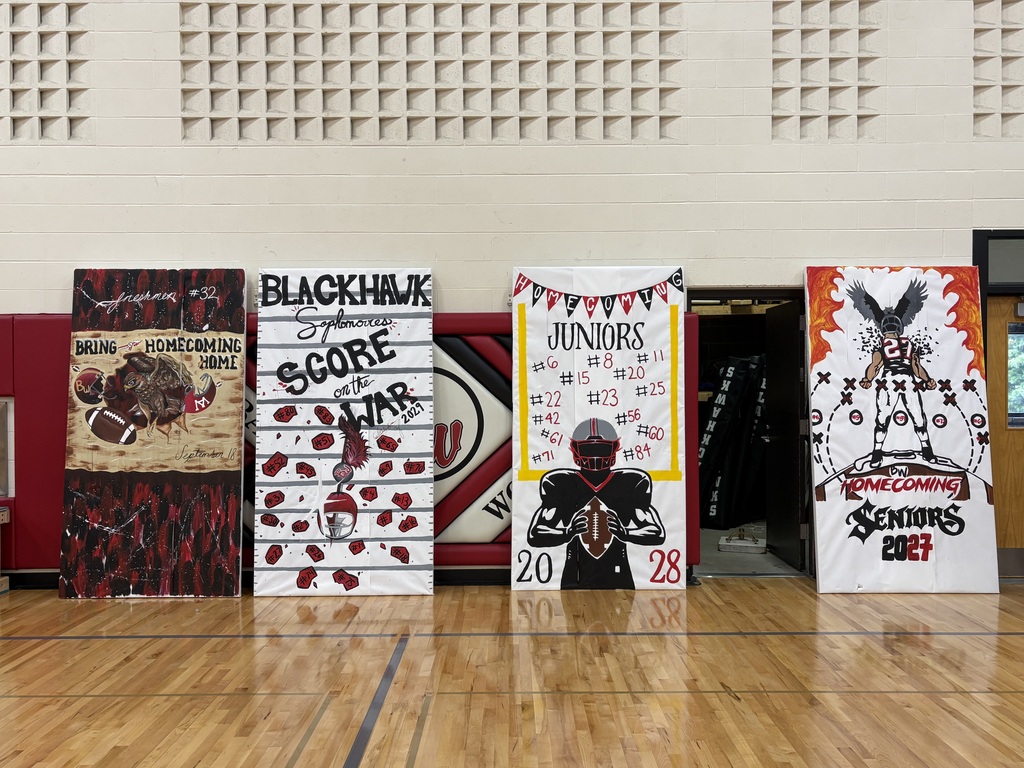 Four hand-painted Homecoming class run-through banners representing the Freshmen, Sophomores, Juniors, and Seniors displayed against the gymnasium wall.