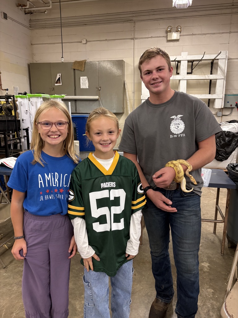 A high school student in a B-W FFA t-shirt holding a snake alongside two smiling younger students, one wearing a Green Bay Packers jersey.