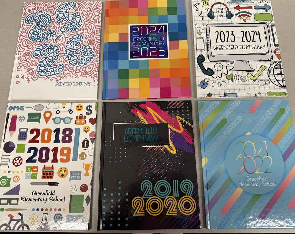 A top-down photograph showing a grid of six different Greenfield Elementary School yearbook covers from recent school years. The covers feature various colorful designs, including school doodles, bright pixel patterns, bold year typography, and colorful circles.