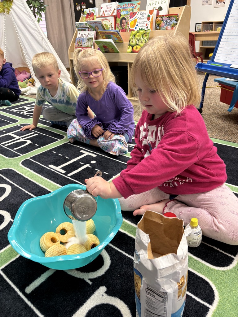 A girl in a pink sweater is pouring ingredients into a bowl over sliced apples.