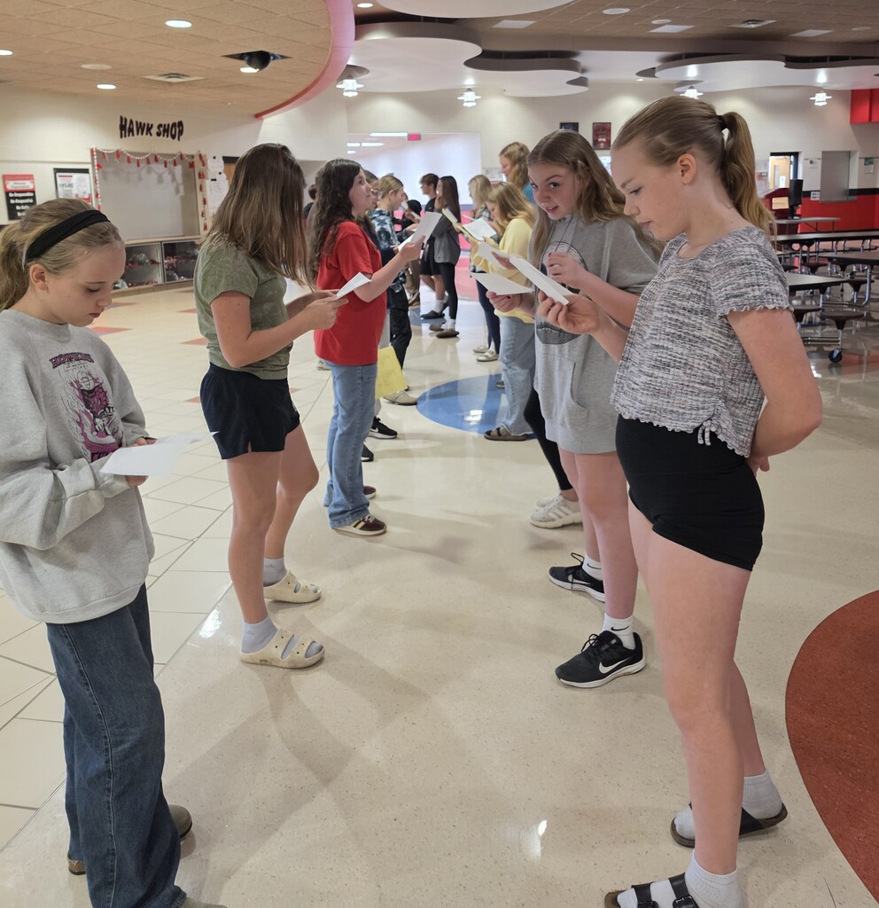 Two long lines of middle school students face each other in the school hallway, holding worksheets and engaging in a Spanish speaking activity with their partners.