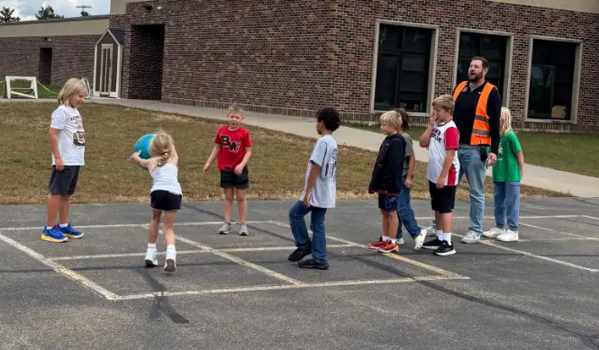 Students and a principal play a game of four-square painted on the outdoor playground blacktop.