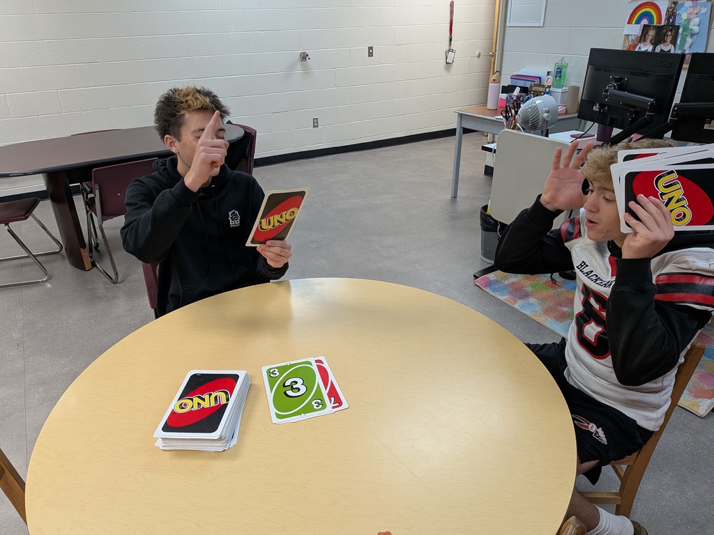 Two male high school students sitting at a round table having fun playing a card game of UNO.