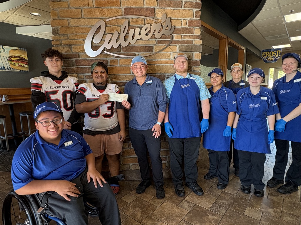 Blackhawks football players Bryce and Sharkie, wearing their #50 and #53 jerseys, standing inside a Culver's restaurant in front of a brick wall and logo alongside Culver's staff members. Sharkie and a Culver's manager are holding up a donation check.
