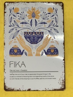 A decorative sign mounted on the wall defining "FIKA" as a Swedish concept for taking time out of your day to appreciate good things, slow down, and enjoy coffee, pastries, and sweet treats with friends.