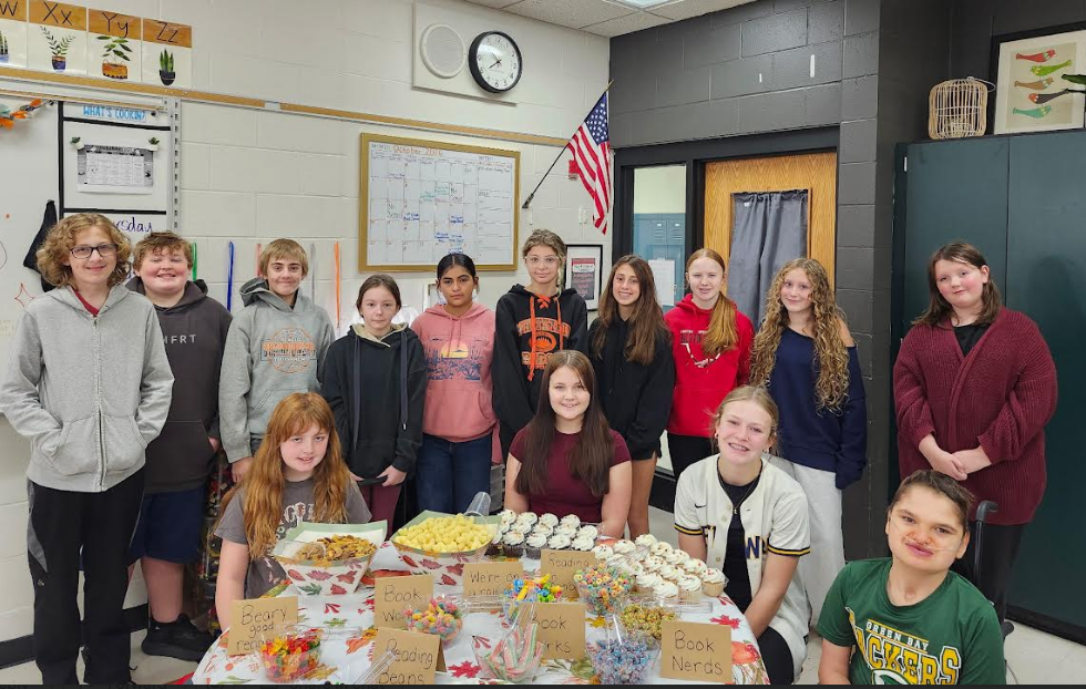 Ms. Varghese’s middle school advisory class gathered together around a snack table covered in cupcakes, treats, and signs with fun reading puns during their Read-a-thon celebration.