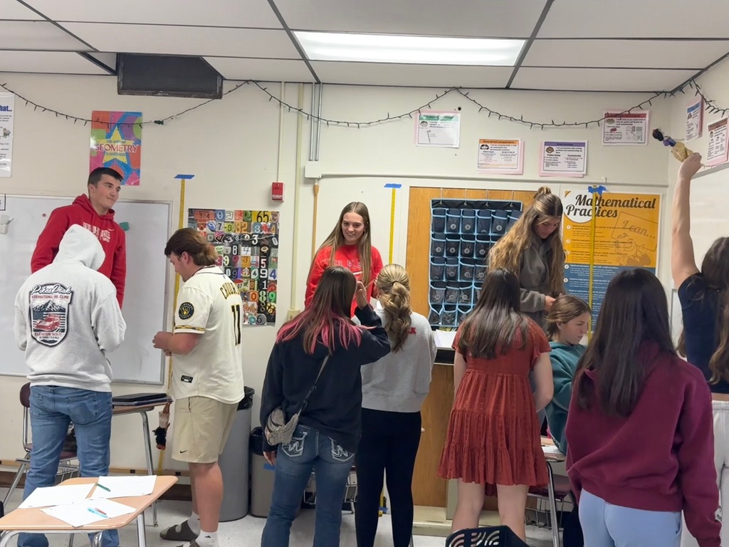 High school students working in small groups in a math classroom during a hands-on lab activity testing rubber band elasticity with dolls.