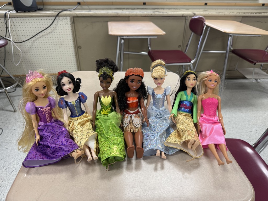 Seven Disney princess Barbie dolls arranged in a row on a school desk, ready for a classroom statistics lab experiment