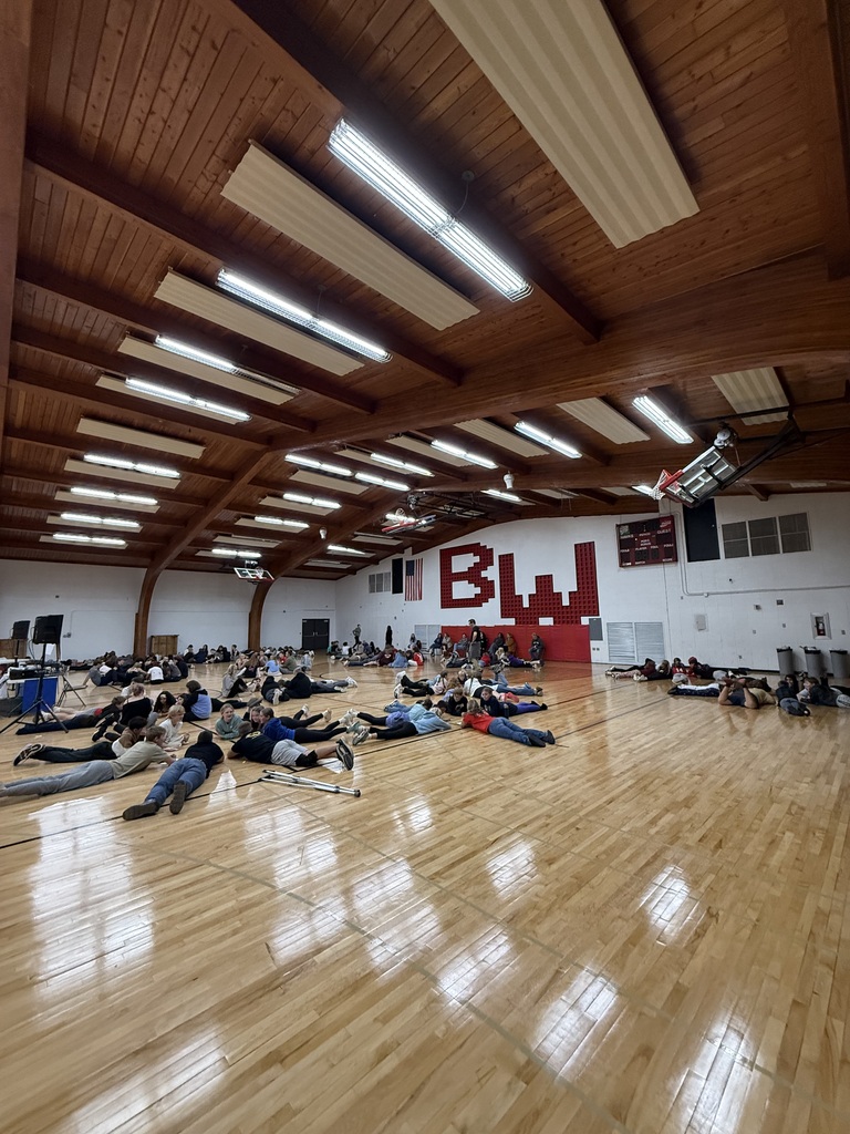 Wide view of the school gymnasium filled with seventh grade students lying on the polished hardwood floor facing forward during a Courage Retreat group exercise.