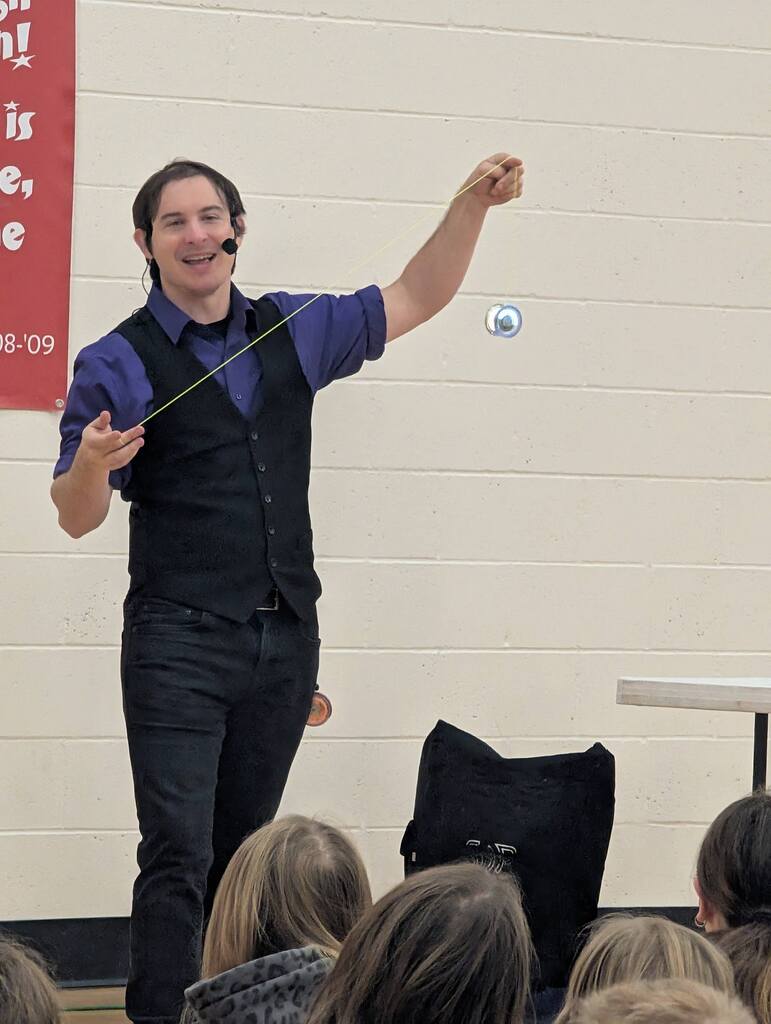 The NED Show performer demonstrates impressive yo-yo tricks in front of a white brick wall for Greenfield Elementary students.