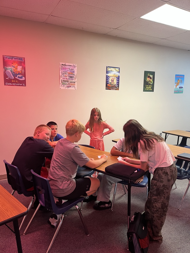 Students sitting and standing around a table working in a classroom on digital citizenship