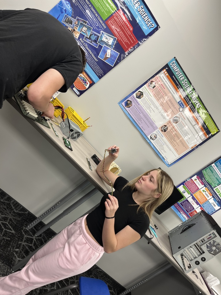Students work together in a computer science classroom, examining cables and components from disassembled desktop computers as part of a hands-on technology activity.