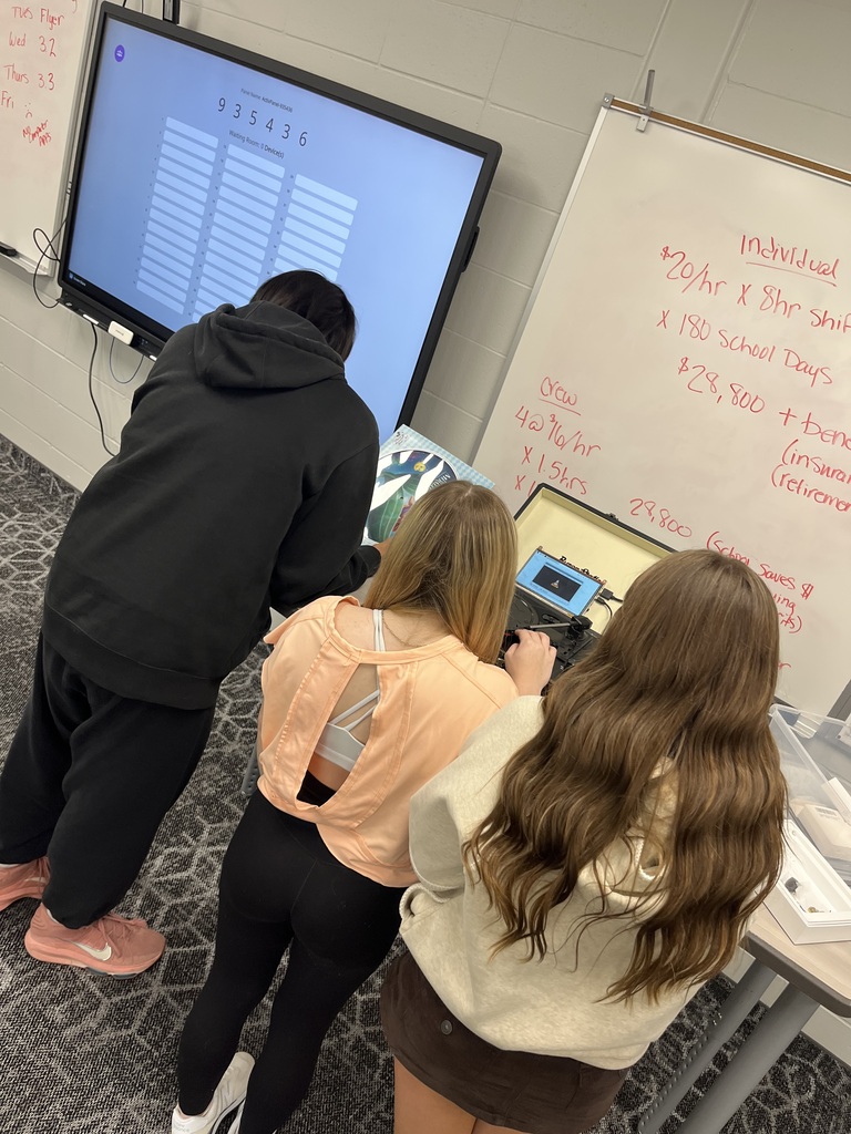 Three students work together at a classroom station with a record player, vinyl record, and small computer while troubleshooting how to play the media.