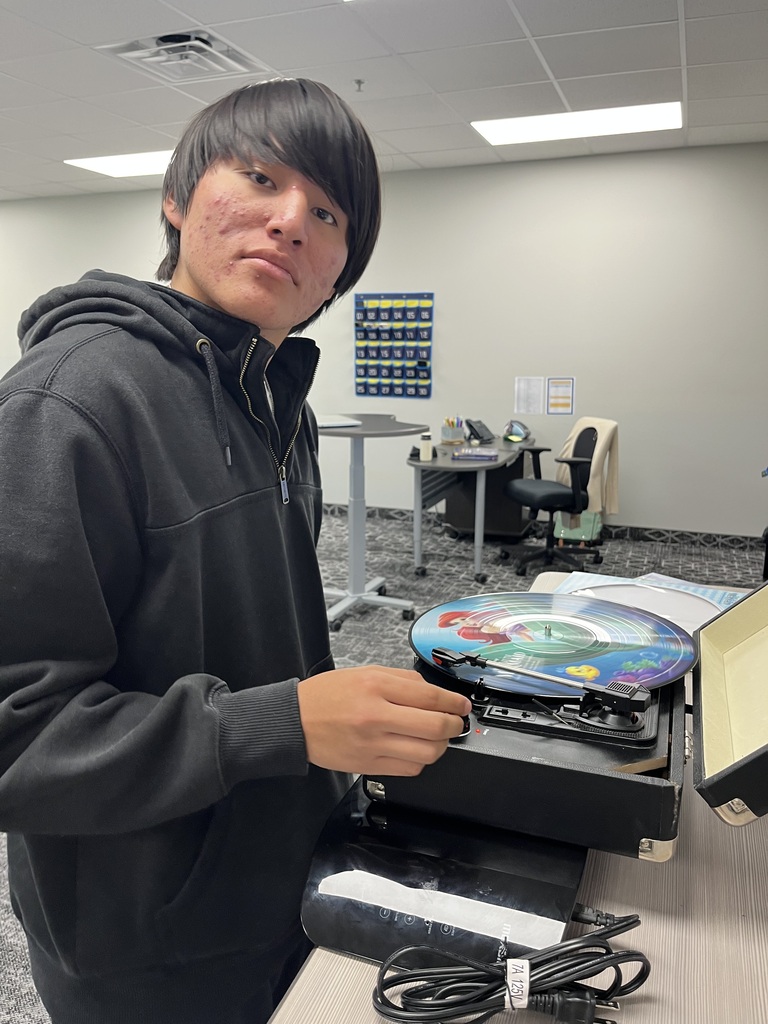 A student operates a portable record player with a colorful vinyl record during a hands-on classroom activity exploring audio technology.